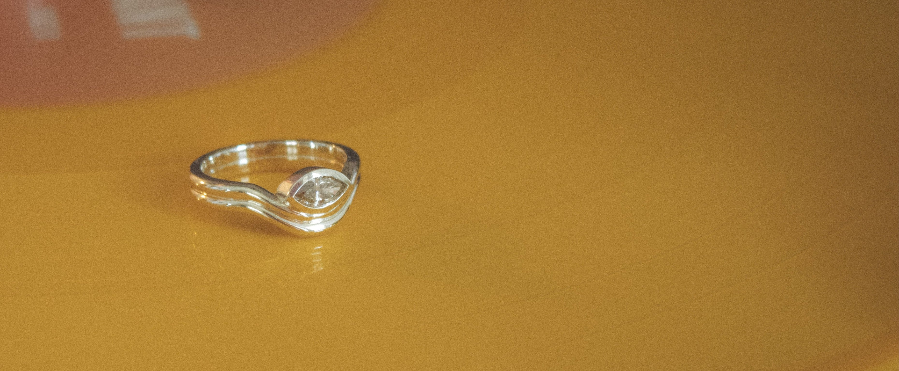 14k gold ring with a bezel set marquise diamond on a yellow surface with a blurred background