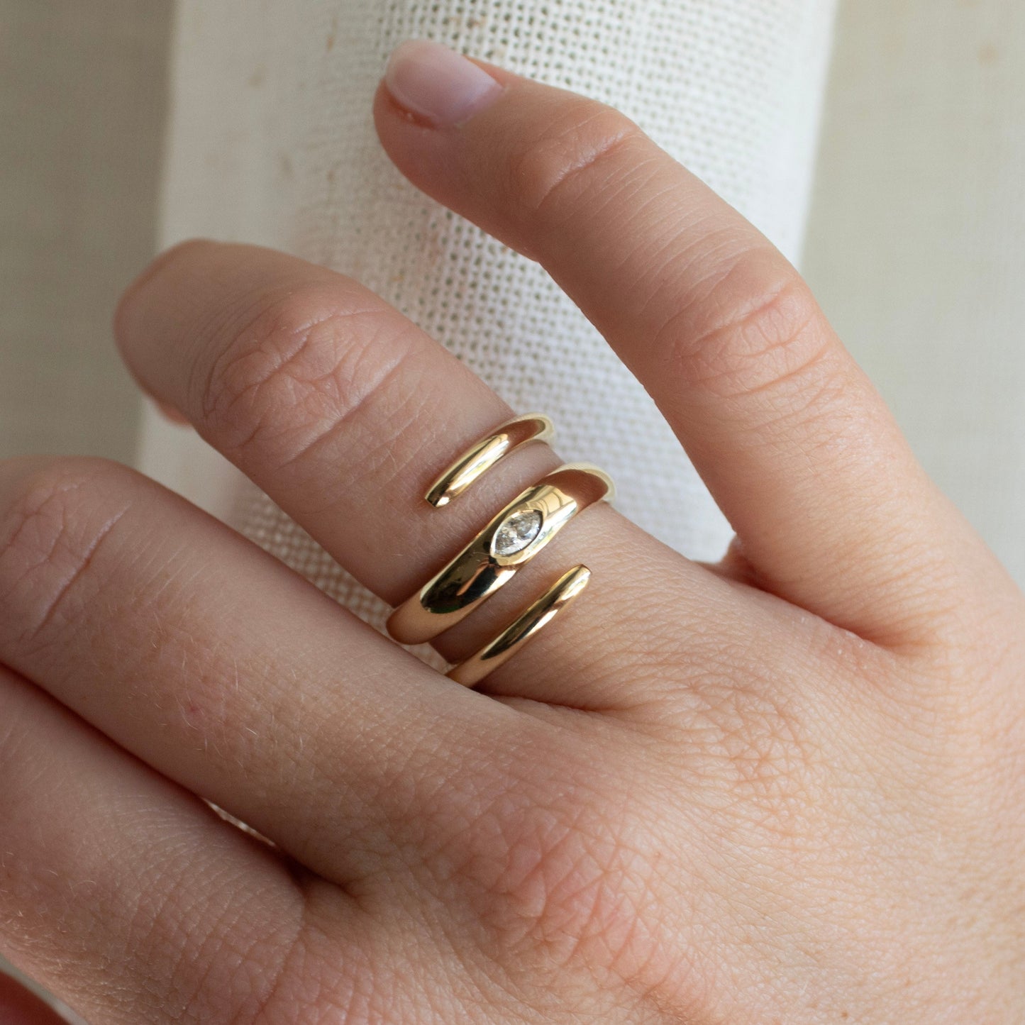 Close-up of a hand wearing a solid 14k yellow gold spiral ring with a lab-grown marquise diamond
