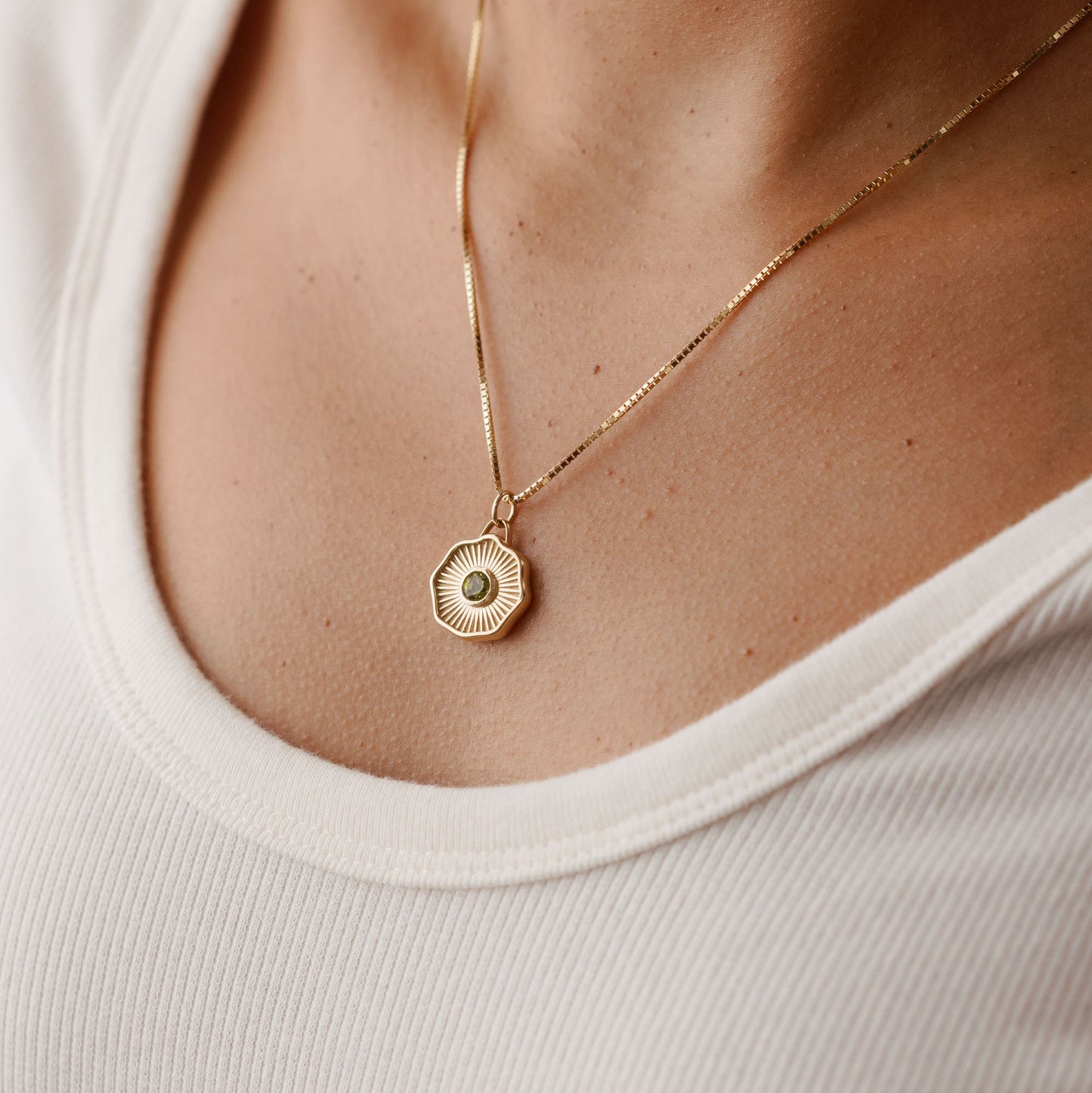 Solid 14k gold pendant with a round bezel-set gemstone being worn