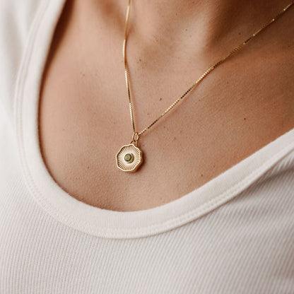 Solid 14k gold pendant with a round bezel-set gemstone being worn
