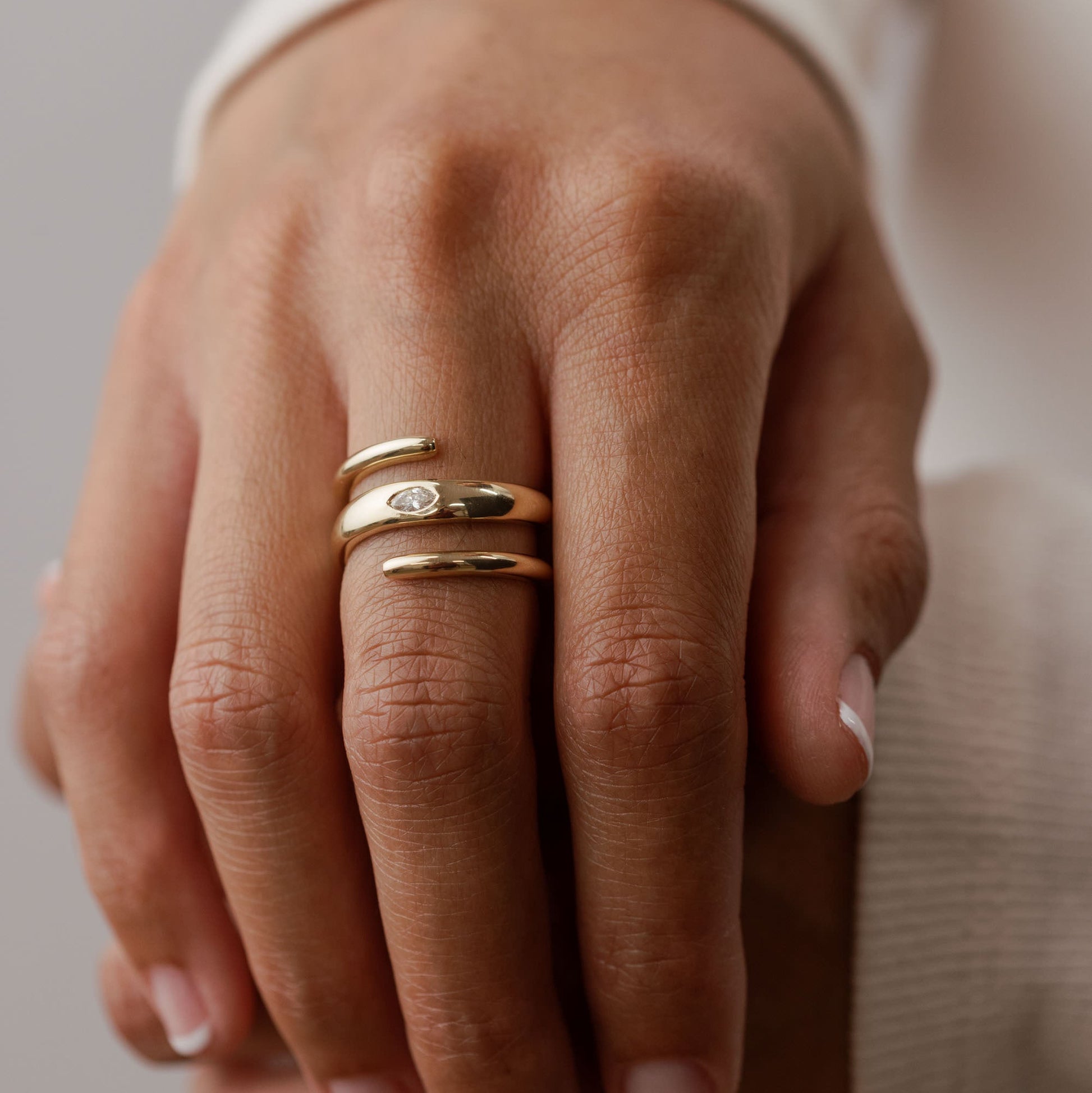Hand wearing 14k solid gold ring with a marquise lab diamond on a neutral background