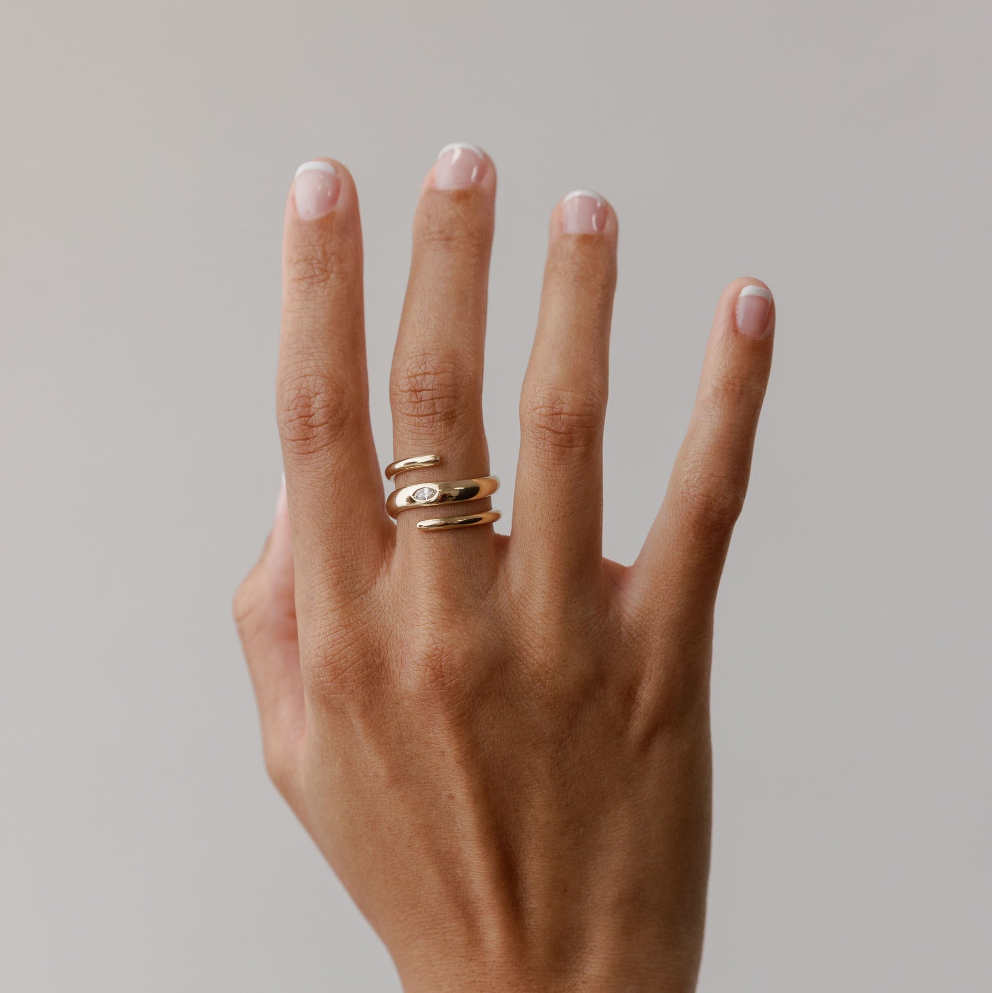 Hand wearing 14k solid gold ring with a marquise lab diamond on a plain background