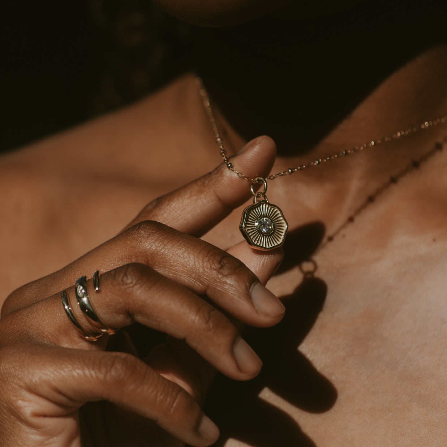Close-up of a hand holding a gold necklace with a pendant against a dark background