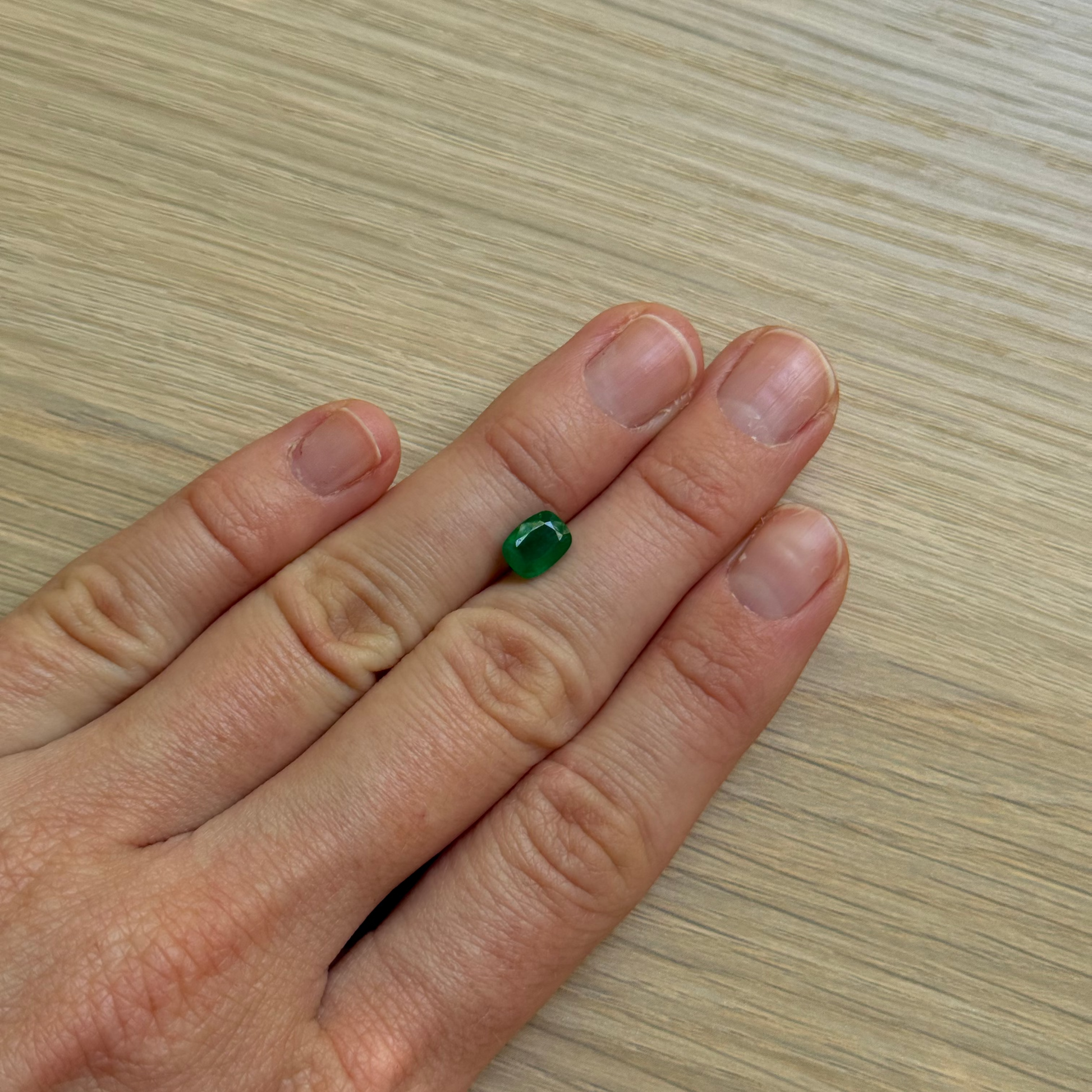 Hand with a green emerald gemstone with a wooden surface background