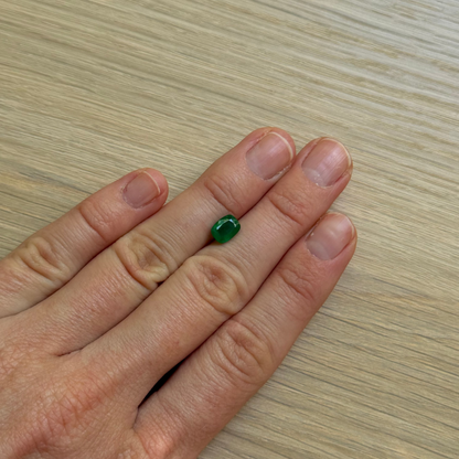 Hand with a green emerald gemstone with a wooden surface background