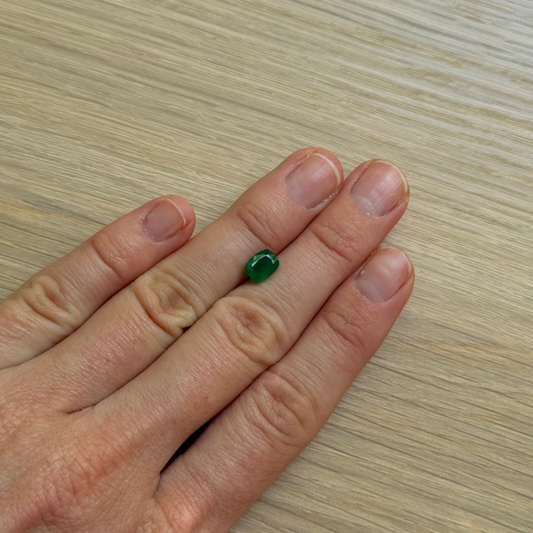 Hand with a green emerald gemstone with a wooden surface background