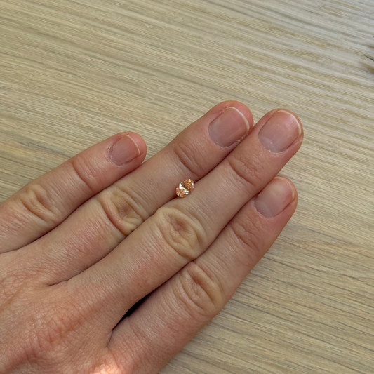 Hand with an oval pink diamond with a wooden surface background