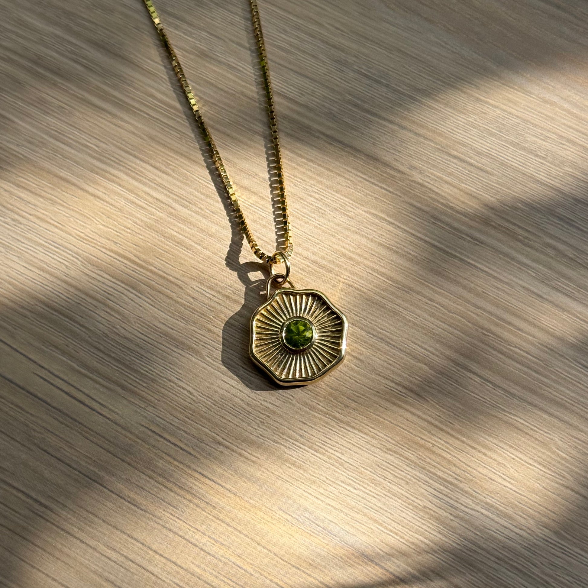 14k solid gold necklace with a green round gemstone pendant on a wooden surface
