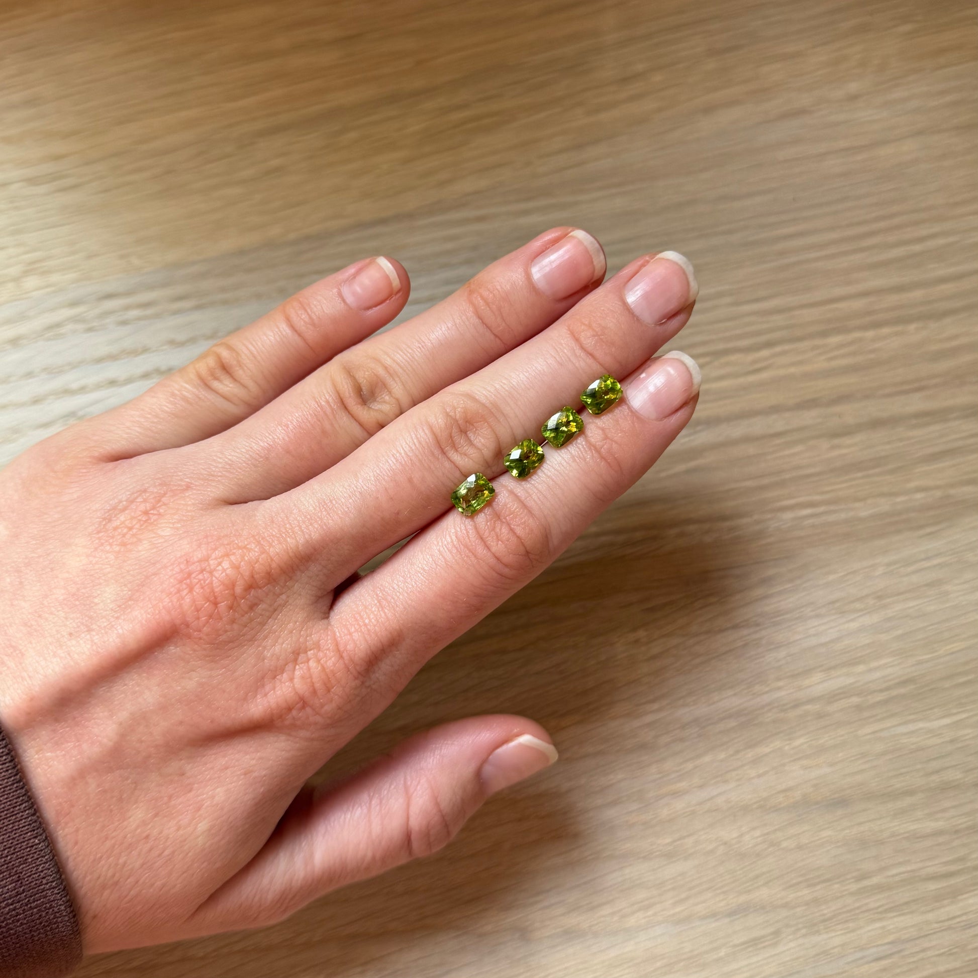 Hand with four green peridot gemstones on a wooden surface