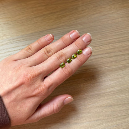 Hand with four green peridot gemstones on a wooden surface