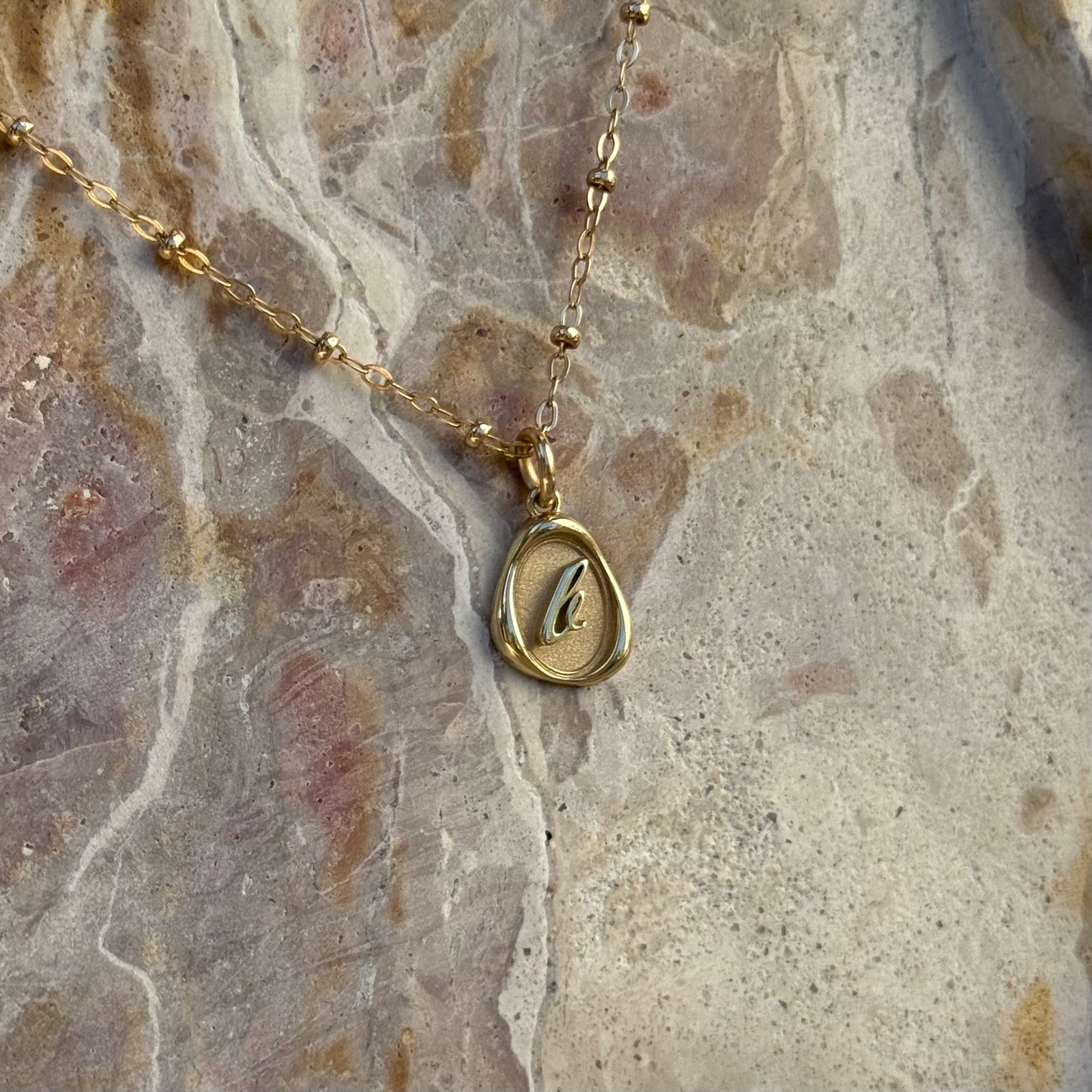 Solid 14k gold charm necklace with custom initial on a stone surface
