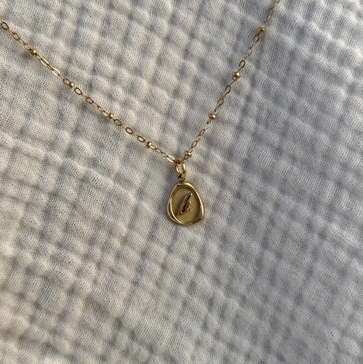 Solid 14k gold charm necklace with custom initial on a facric background