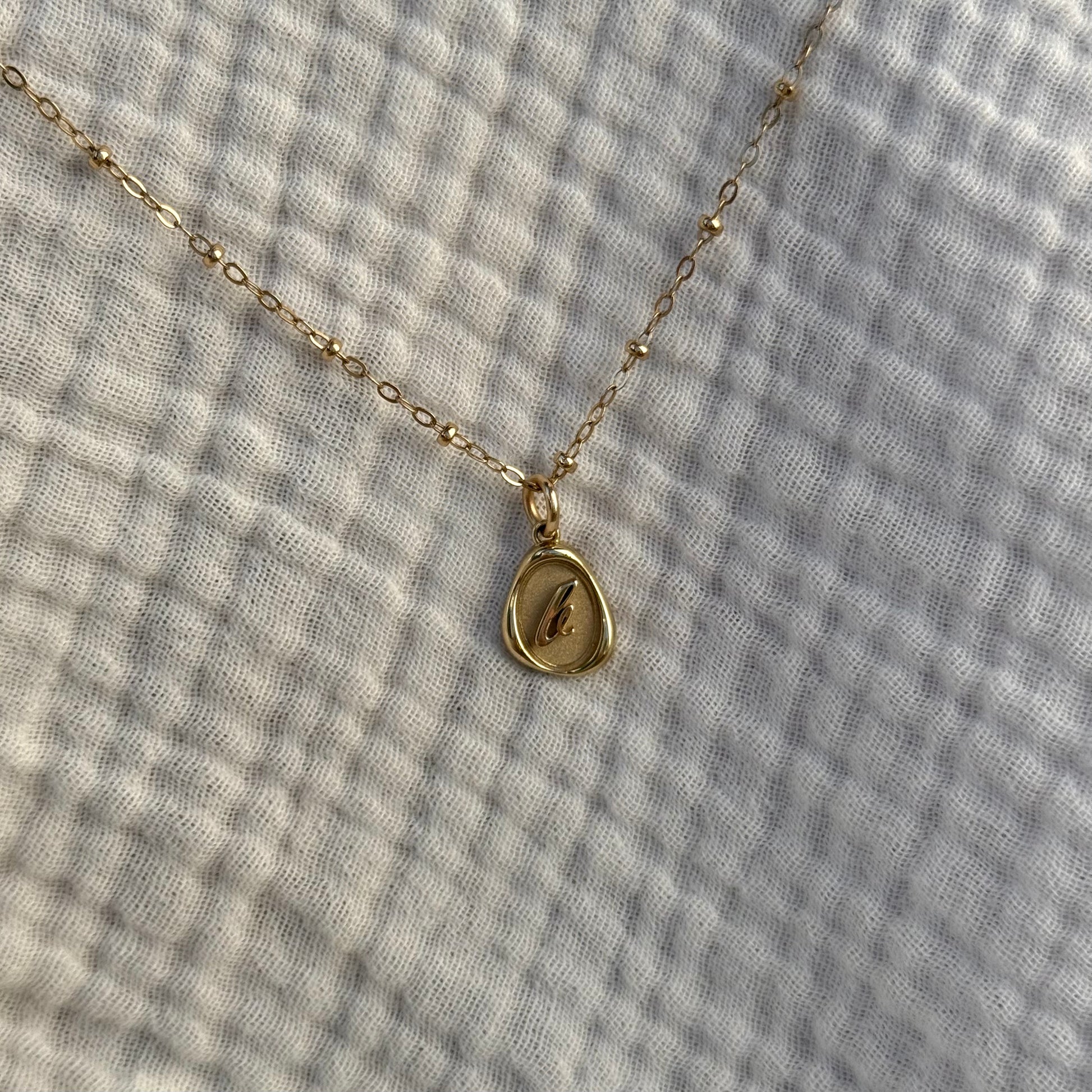 Solid 14k gold charm necklace with custom initial on a facric background