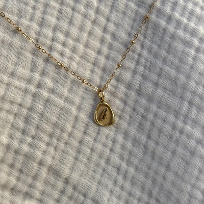 Solid 14k gold charm necklace with custom initial on a facric background