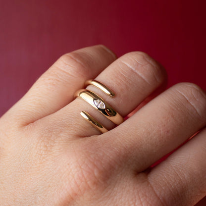 Close-up of a hand wearing a solid 14k yellow gold spiral ring with a lab-grown marquise diamond on a red background