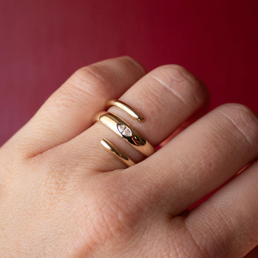 Close-up of a hand wearing a solid 14k yellow gold spiral ring with a lab-grown marquise diamond on a red background