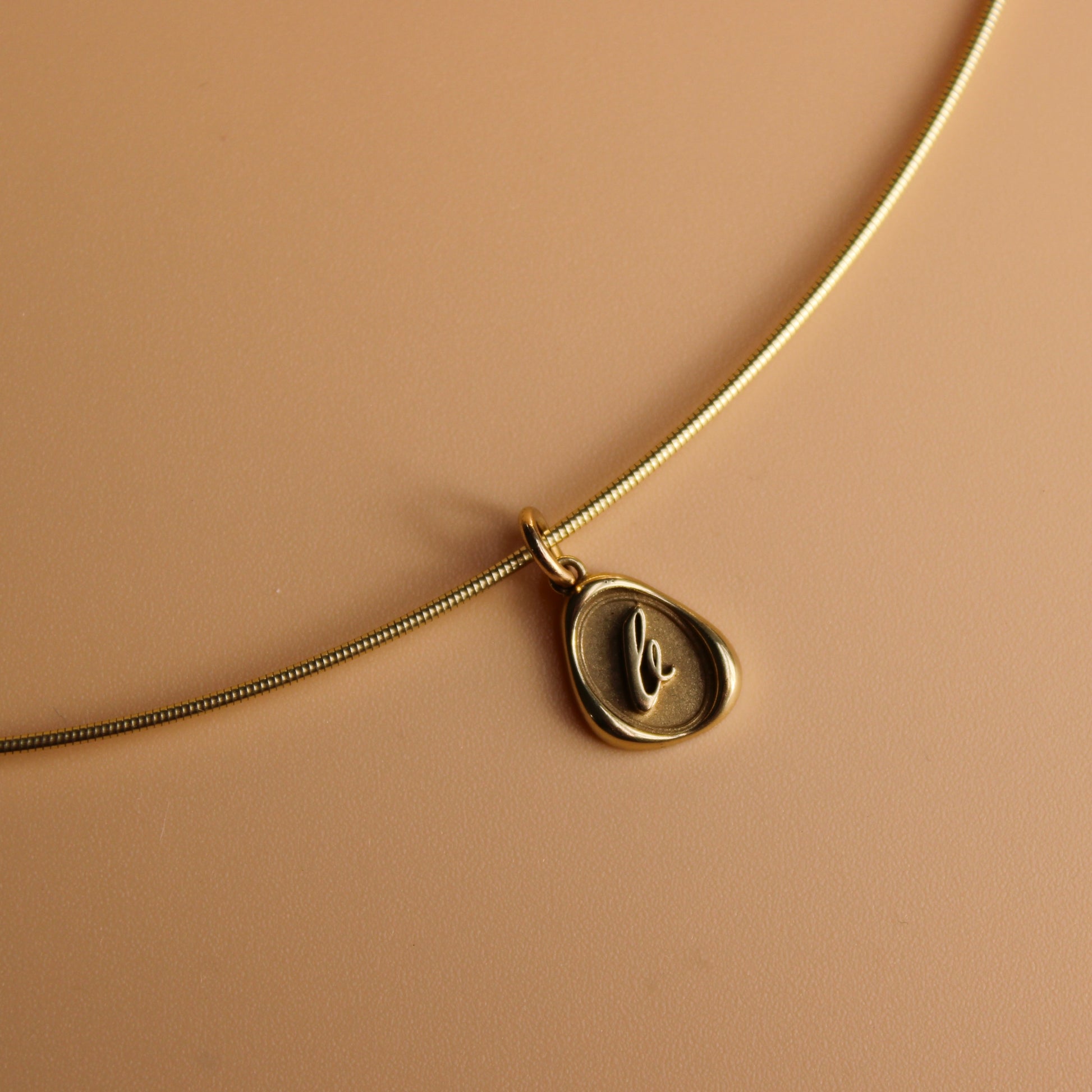 Gold omega chain with a wax seal charm on a beige background