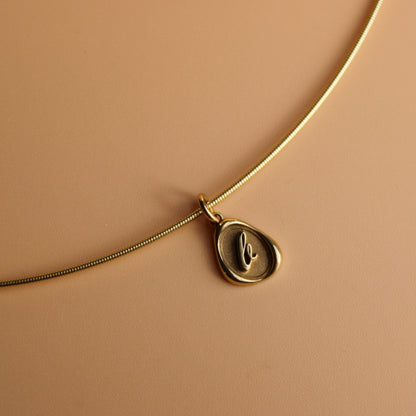 Gold omega chain with a wax seal charm on a beige background