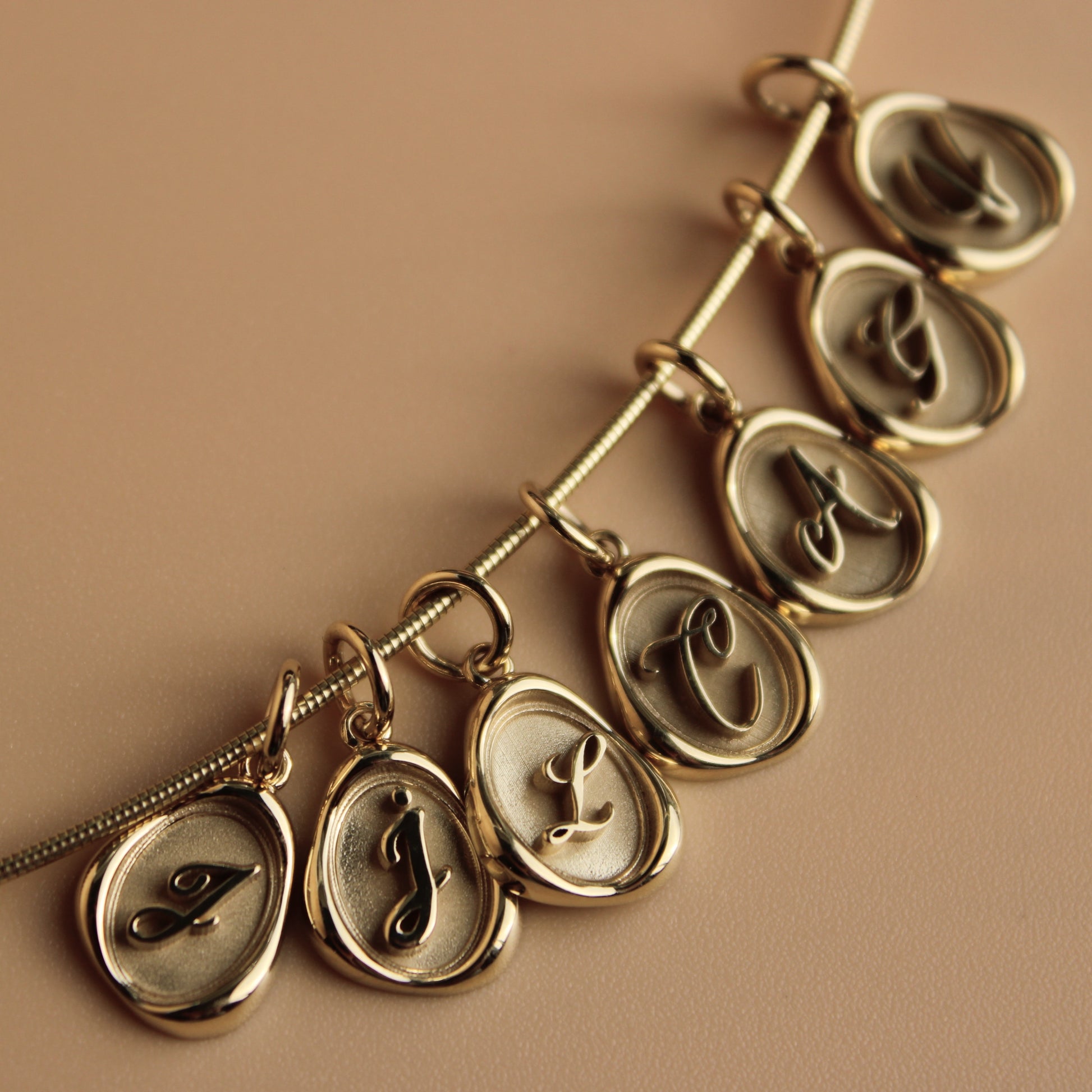 Gold omega necklace chain with wax seal charms on a beige background