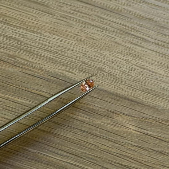 Tweezers holding an oval pink diamond with a wooden surface background