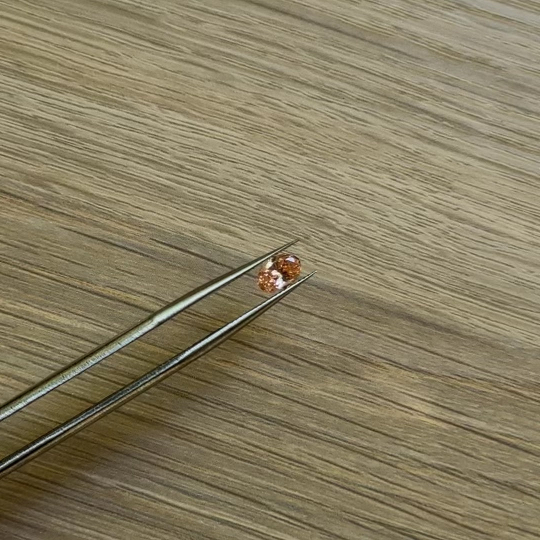 Tweezers holding an oval pink diamond with a wooden surface background