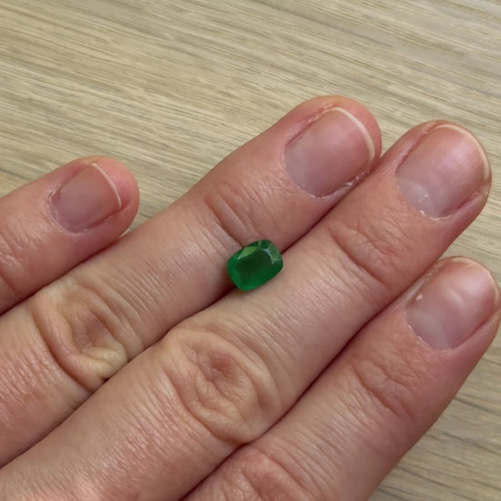 Hand with a green emerald gemstone with a wooden surface background