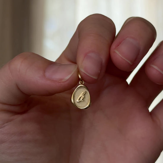 Solid 14k gold charm necklace with custom initial being held 