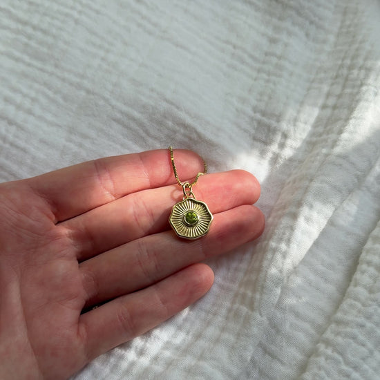 Solid 14k gold necklace with a green gemstone pendant on a cloth background