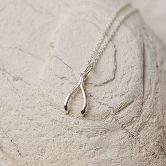 A sterling silver wishbone charm necklace resting on a textured surface.